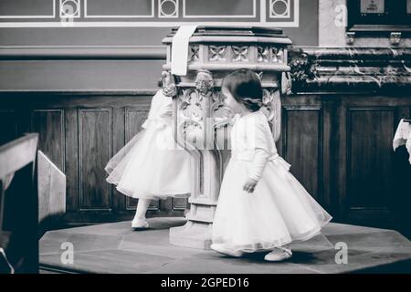 Une photo en niveaux de gris de petites filles caucasiennes miettes dans des robes blanches jouant au coin de la pièce Banque D'Images