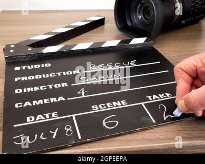 Gros plan POV tourné de la main d'un homme à craquer prendre 2 sur un tableau de clapper traditionnel, avec une caméra vidéo derrière. Banque D'Images