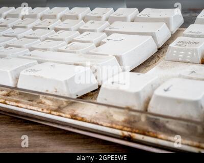 Gros plan POV d'un clavier d'ordinateur blanc sale crasseux sur un bureau. Banque D'Images