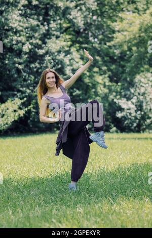 Une fille souriante en costume de hip-hop lilas en danse pose sur la pelouse dans le parc Banque D'Images