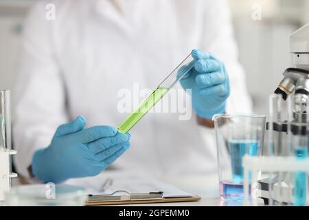 Le scientifique en gants de protection maintient le tube à essai avec un écran de fermeture de liquide vert Banque D'Images