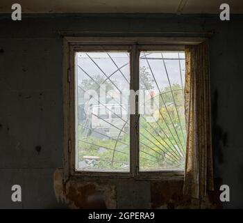 Vieille fenêtre sale avec des rideaux en lambeaux dans l'intérieur ancien bâtiment abandonné. Banque D'Images