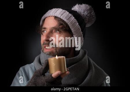 Homme caucasien d'âge moyen portant des gants sans doigts et un chapeau tricoté et tenant une bougie Banque D'Images