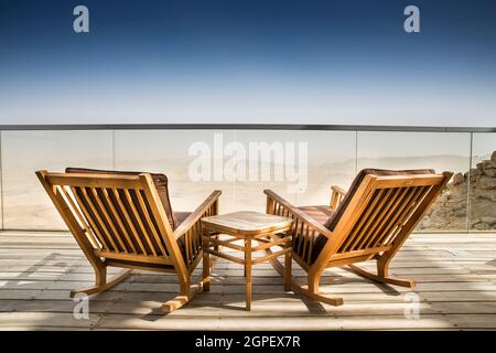 Transats sur une terrasse en bois donnant sur un vaste paysage stérile. Photographié au Ramon Creater, désert du Néguev, Israël Banque D'Images
