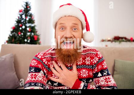 Photo de bonne humeur souriante stupéfait homme dans le chapeau de santa main main poitrine écouter des nouvelles inattendues information célébrer le nouvel an Banque D'Images