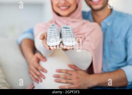 Concept de planification familiale. De jolies chaussures de bébé dans les mains des couples musulmans enceintes, homme et femme montrant de petites chaussures pour leur bébé Banque D'Images