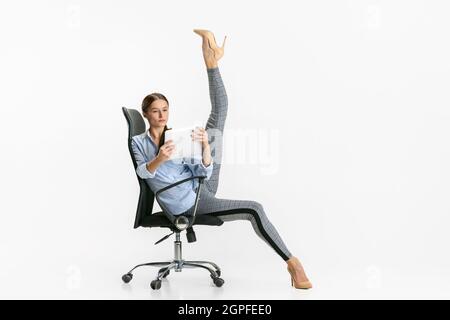 Portrait d'une femme, employée de bureau debout sur une chaise en posture de ballet et lecture à partir d'une tablette isolée sur fond blanc Banque D'Images