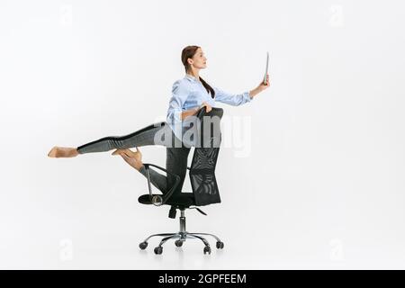 Portrait complet d'une femme, employée de bureau debout sur une chaise en posture de ballet et lecture à partir d'une tablette isolée sur fond blanc Banque D'Images