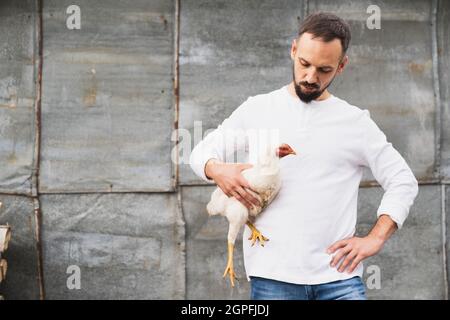 Le fermier tient le poulet dans ses bras et le regarde Banque D'Images