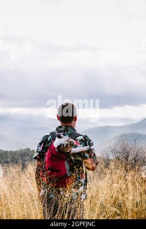 Vue arrière du voyageur avec chien dans le sac à dos au sommet de la montagne Banque D'Images