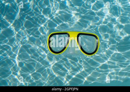 Un masque de plongée jaune flottant dans une piscine bleu clair et ondulée Banque D'Images