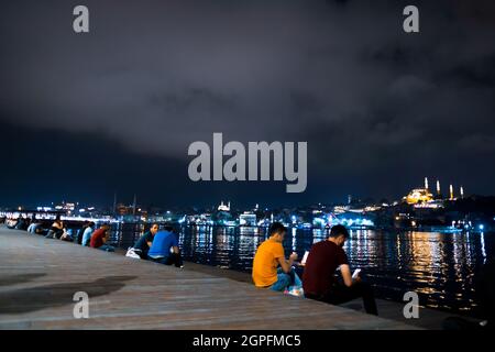 Beyoglu, Istanbul, Turquie - 07.07.2021: Les Turcs assis la nuit sur la côte de Karakoy et regardant le paysage marin près de la Corne d'Or et les lumières de la ville shin Banque D'Images