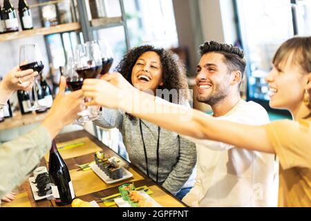 Des amis souriants et multiculturels dégustent du vin rouge au restaurant du bar à sushis - concept de mode de vie gastronomique avec des jeunes qui s'amusent ensemble à tout moment Banque D'Images