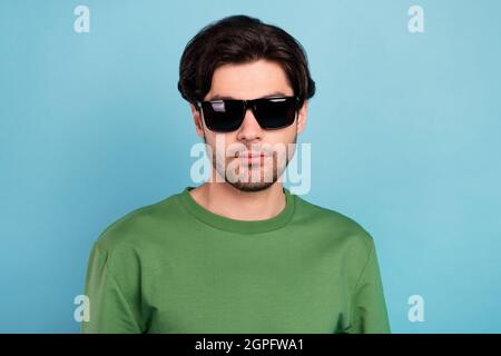 Portrait de beau sérieux homme paisible porter un pull-over vert de verre solaire isolé sur fond bleu de couleur Banque D'Images