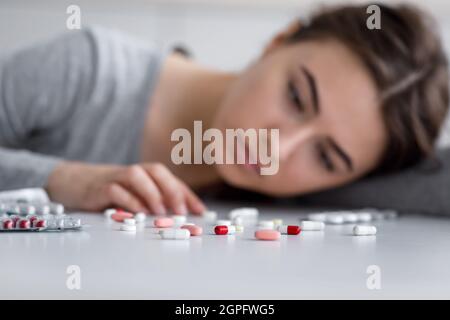 Gros plan portrait du désespoir déprimé caucasiens millénaire jolie femelle couché sur le sol et regarder des médicaments Banque D'Images