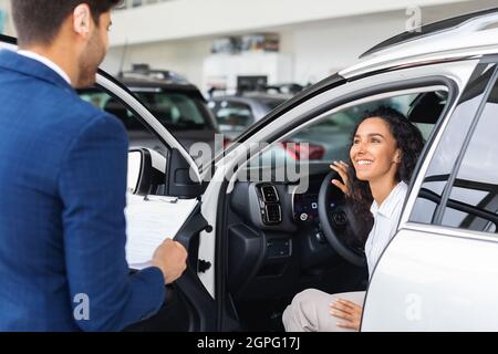 Jeune femme joyeuse assise à l'intérieur d'une voiture neuve Banque D'Images