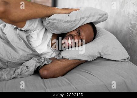 Homme noir stressé couvrant les oreilles couchées dans le lit Banque D'Images