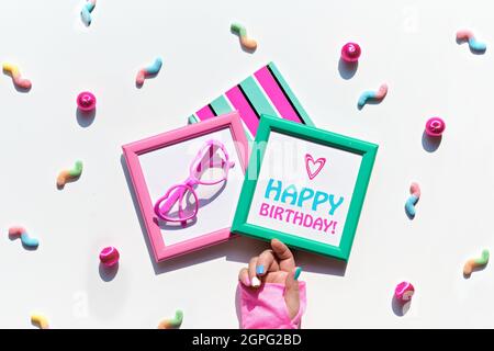 Envoyez un texte « Joyeux anniversaire » avec des bonbons et des objets de décoration de fête éclatants. Bonbons, en-cas sucrés, gaz en forme de coeur drôle dans les cadres d'image. Géométrique festif Banque D'Images
