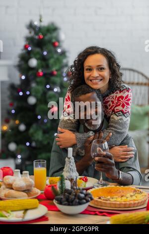 bonne femme afro-américaine embrassant papa tenant un verre de vin rouge pendant le dîner de noël Banque D'Images