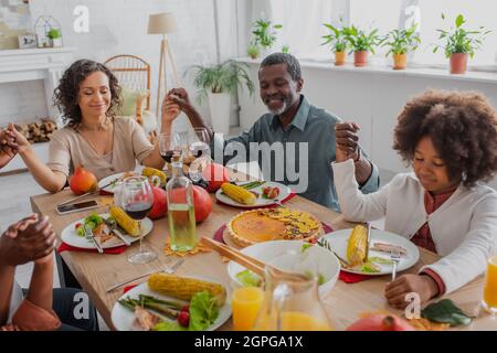 bonne famille afro-américaine se tenant les mains tout en priant avant le dîner d'action de grâce Banque D'Images