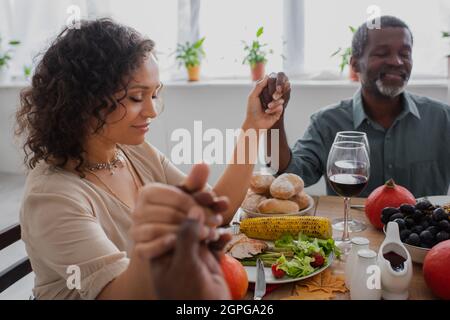 femme afro-américaine tenant la main avec les parents tout en priant avant de dîner d'action de grâce avec les yeux fermés Banque D'Images