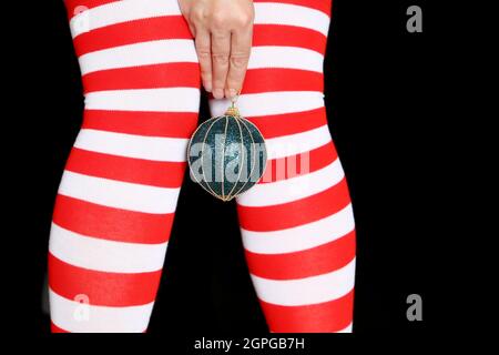 Jambes de femme en chaussettes de Noël sur fond noir. Femme avec balle de jouet en main, concept de célébration du nouvel an, fille en costume de Santa Banque D'Images