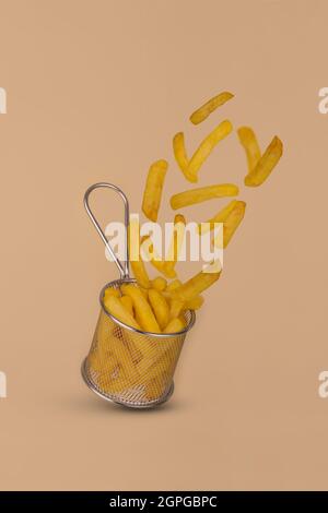 Frites - pommes de terre frites sortant du panier. Les fast-foods se levent sur fond beige. Concept alimentaire créatif. Banque D'Images