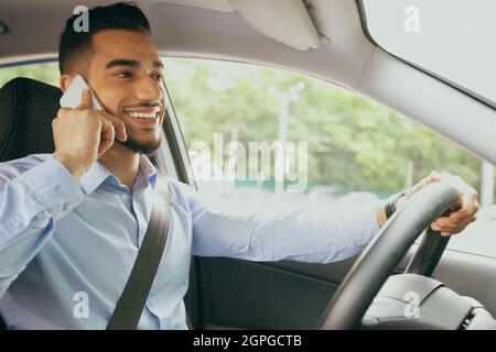 Homme arabe positif ayant une conversation téléphonique en conduisant la voiture Banque D'Images