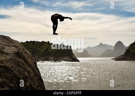 Silhouette d'un Buy saut dans l'océan avec la montagne de Sugarloaf et Corcovado sur fond, à Niteroi, Rio de Janeiro, Brésil Banque D'Images