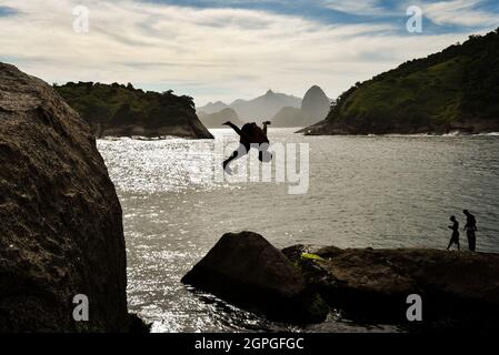 Silhouette d'un Buy saut dans l'océan avec la montagne de Sugarloaf et Corcovado sur fond, à Niteroi, Rio de Janeiro, Brésil Banque D'Images