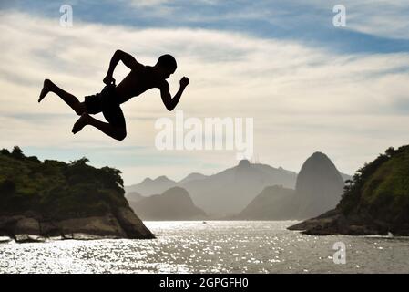 Silhouette d'un Buy saut dans l'océan avec la montagne de Sugarloaf et Corcovado sur fond, à Niteroi, Rio de Janeiro, Brésil Banque D'Images