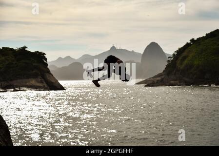 Silhouette d'un Buy saut dans l'océan avec la montagne de Sugarloaf et Corcovado sur fond, à Niteroi, Rio de Janeiro, Brésil Banque D'Images