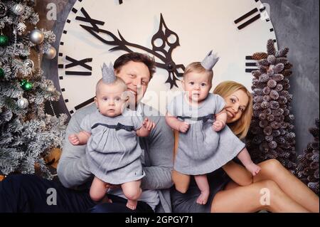 Une grande famille heureuse avec des enfants jumeaux dans l'intérieur de la maison du nouvel an sur fond d'une grande horloge. Banque D'Images