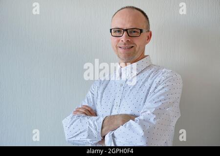 Vue en demi-longueur d'un homme souriant et non rasé.Un homme d'âge moyen avec des lunettes se tient contre un fond blanc.La photo inclut un espace de copie Banque D'Images