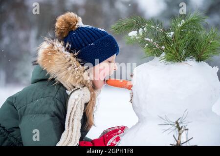 Blonde mignonne fille heureux enfant mangeant bonhomme de neige nez de carotte Banque D'Images