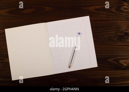 Carnet d'école avec lignes obliques, stylo transparent sur la table marron fond de bois. Feuille de papier vierge dans le carnet du bureau. Retour à l'école Banque D'Images