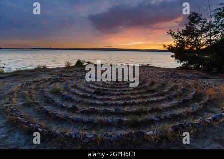 Labyrinthe en spirale fait de pierres sur la côte au coucher du soleil Banque D'Images