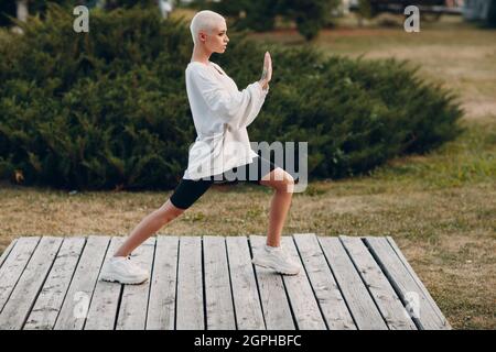 Portrait d'une jeune femme européenne à poil court souriant faisant du Qigong Taijiquan dans un parc d'été. Belle fillette blonde heureuse en plein air. Banque D'Images