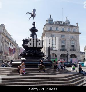 Londres, Grand Londres, Angleterre, 21 septembre 2021 : Tourses, assis et sourire, et chat sur la fontaine commémorative Shaftesbury alias Eros dans Piccadilly Circus. Banque D'Images