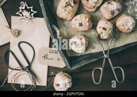 Mini-Stollen avec glaçage au sucre sur un plateau en bois, sacs en papier, ciseaux et ruban cadeau sur bois sombre, scène pour la préparation des cadeaux de l'Avent ou de noël, dessus Banque D'Images