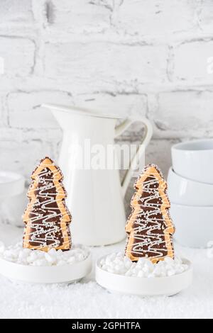 Deux biscuits en forme d'arbres de noël avec glaçage au chocolat et au sucre dans des bols avec du sucre grossier sur fond blanc, vertical avec espace de copie Banque D'Images