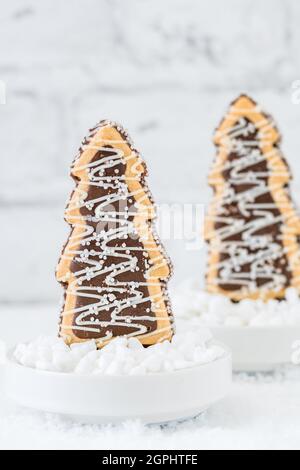 Deux biscuits en forme d'arbres de noël avec glaçage au chocolat et au sucre dans des bols avec du sucre grossier sur fond blanc, vertical avec espace de copie Banque D'Images