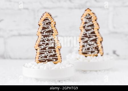 Deux biscuits en forme d'arbres de noël avec glaçage au chocolat et au sucre dans des bols avec du sucre grossier sur fond blanc Banque D'Images