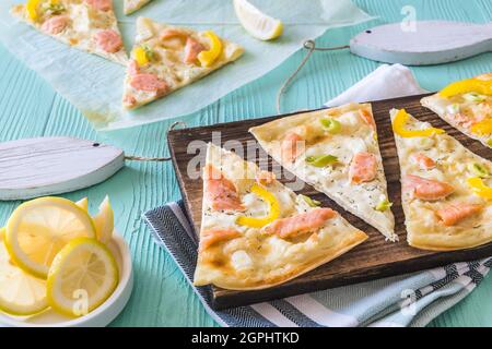 Morceaux de tarte flambé au saumon, au poivre jaune et aux ciboules sur un panneau de bois sur fond vert clair Banque D'Images