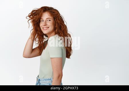 Style de vie et personnes. Jolie fille en forme de candive avec des cheveux rouges et des taches de rousseur, jouant avec la coupe de cheveux et souriant heureux à l'appareil photo, debout dans le tee-shirt plus Banque D'Images