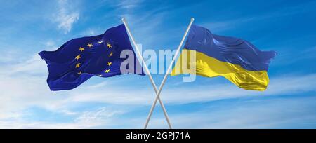 Drapeaux de l'Union européenne et de l'Ukraine agitant dans le vent sur des mâts de drapeaux contre le ciel avec des nuages le jour ensoleillé. Symbolisant la relation, le dialogue entre deux Banque D'Images