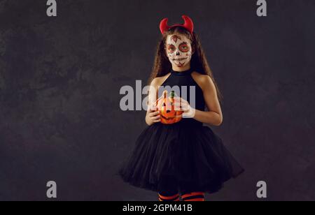 Portrait studio d'une petite fille avec un maquillage de crâne tenant une citrouille d'Halloween Banque D'Images