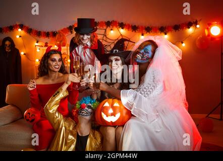 Groupe d'amis gaies dans des costumes effrayants d'halloween posant avec des verres de champagne dans les mains. Banque D'Images