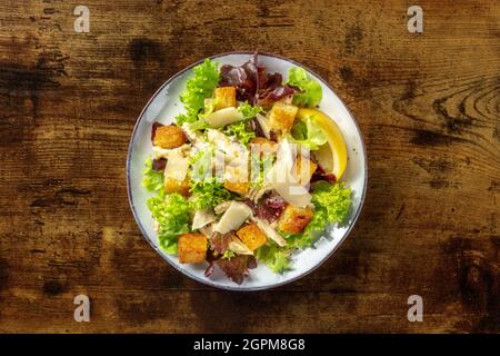 Salade César au poulet, prise en tête sur fond de bois rustique foncé. Feuilles de Romaine, croûtons croustillants et viande de poulet au filet Banque D'Images