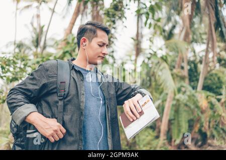 homme avec sac à dos tenir la carte en vérifiant le temps le bus et lui et de marcher sur la route dans la forêt. Concept de voyage à dos. Banque D'Images